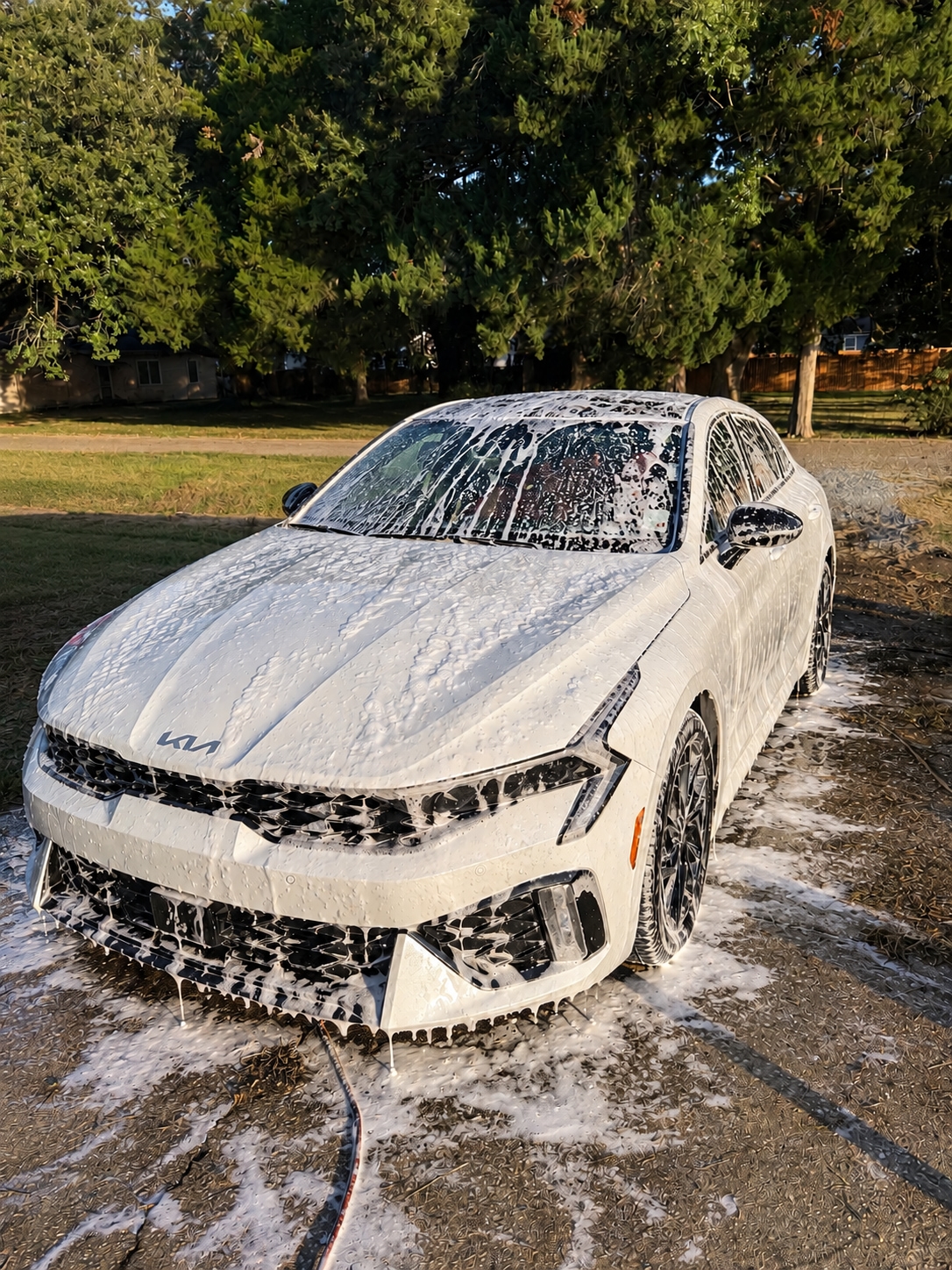 White Kia K5 covered in soap foam during an exterior detail
